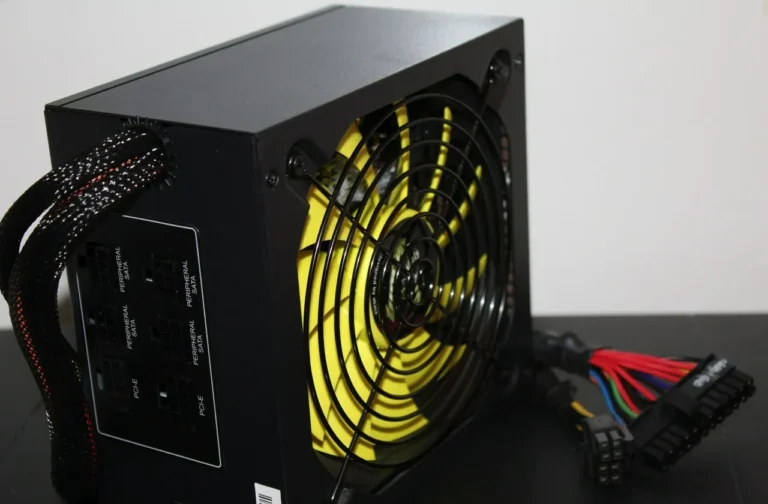 Imagem mostrando fonte de PC preta nova, com ventoinhas amarelas, e cabos da placa mãe conectados no conectador a vista, sobre uma superfície preta. O fundo é branco. Como testar fonte de PC.