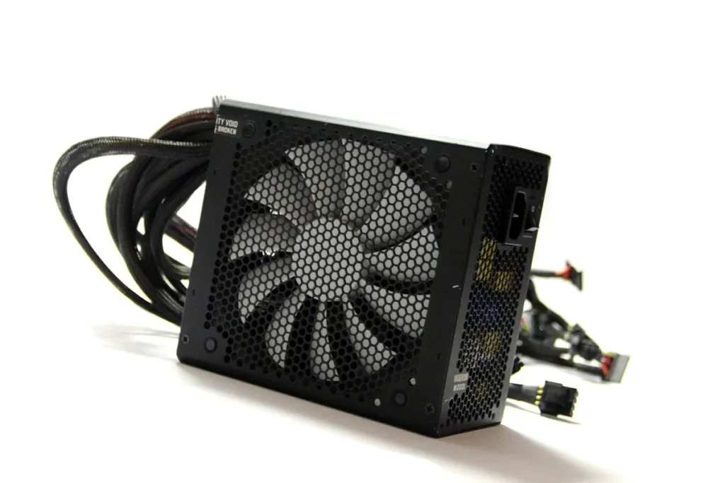 Página Inicial - Guru Recomenda 80 Imagem representando a melhor fonte para PC de 2024. Fonte de PC preta vista de lado sobre superfície branca, onde podemos observar o ventilador. Da parte de trás saem os cabos, que estão posicionados do outro lado da fonte. As ponteiras são coloridas, e os cabos são pretos. O fundo é branco.