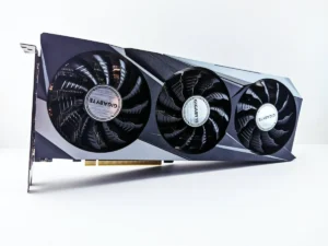Melhor Pasta Térmica: TOP 10 Melhores (Cooler, Master, Grizzly e mais) 44 Placa de vídeo com partes prateadas e partes em preto fosco, com 3 ventiladores pretos., colocada na horizontal sobre superfície branca. O fundo é branco. Melhores placas de vídeo 2024.